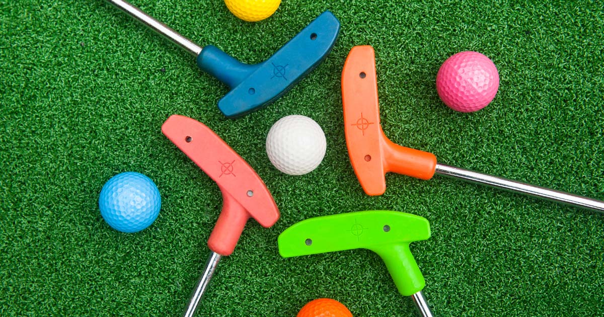 Multiple colorful mini golf clubs laying on green turf beside several golf balls