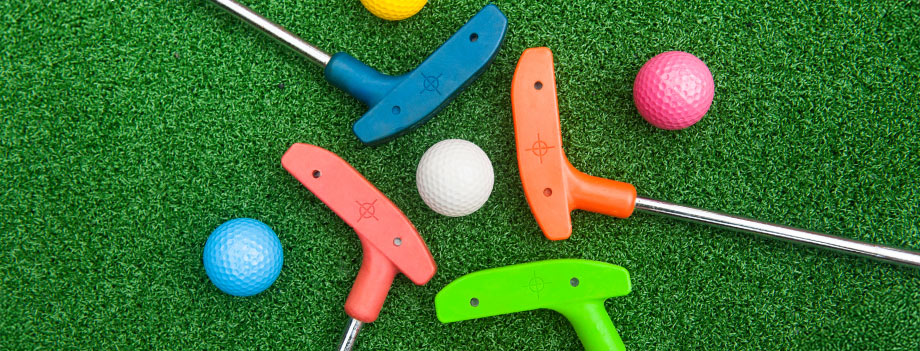Multiple colorful mini golf clubs laying on green turf beside several golf balls