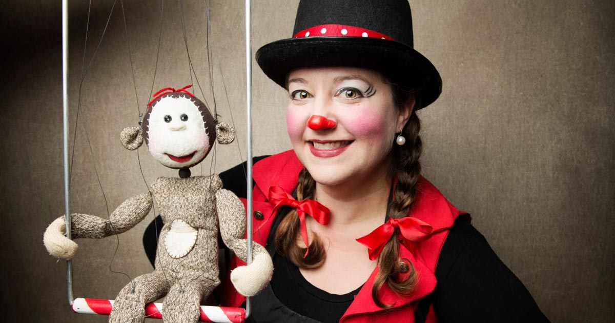 Cast member dressed like a clown posing with a monkey sock puppet